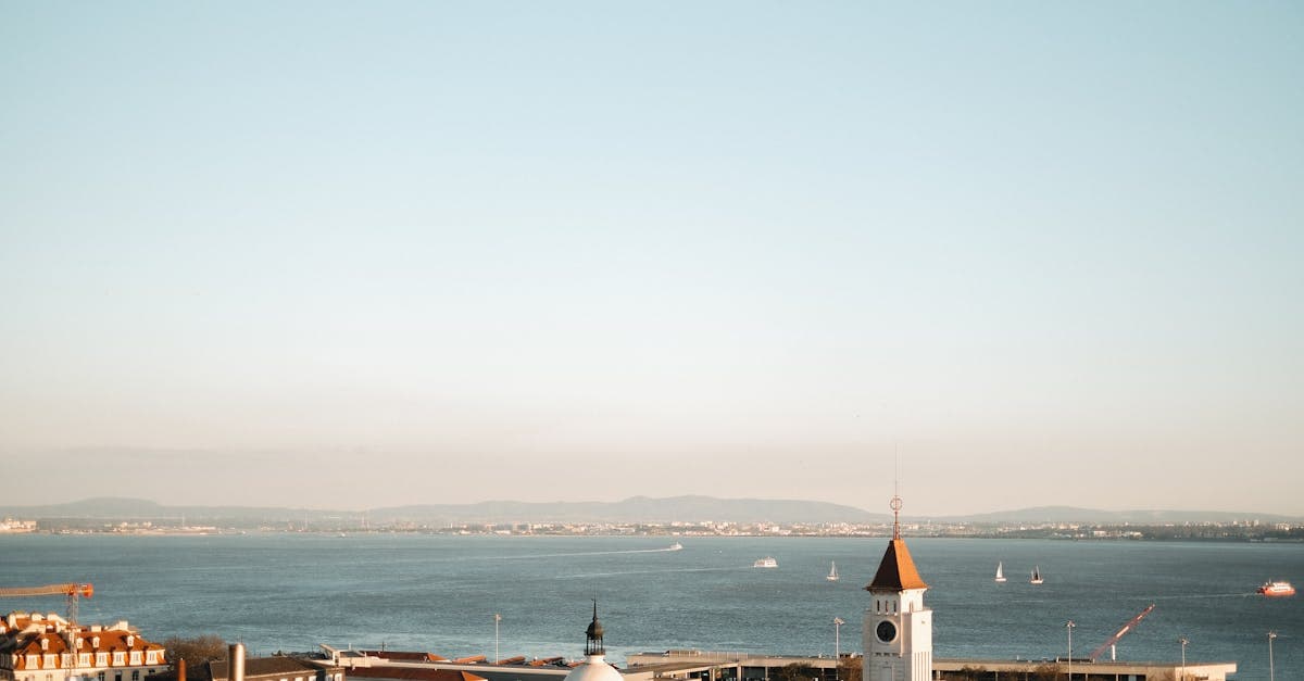 A scenic view of a coastal town with a clock tower overlooking the calm ocean and sailboats.