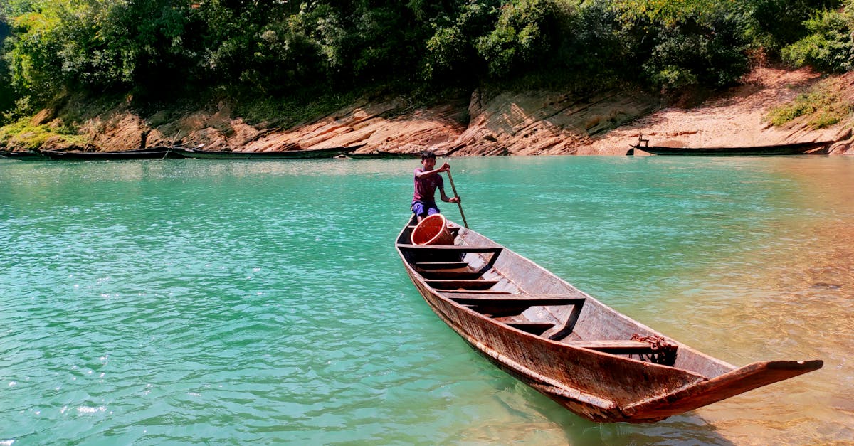 A person rowing a wooden boat on turquoise waters surrounded by lush greenery in Chattogram, Bangladesh.