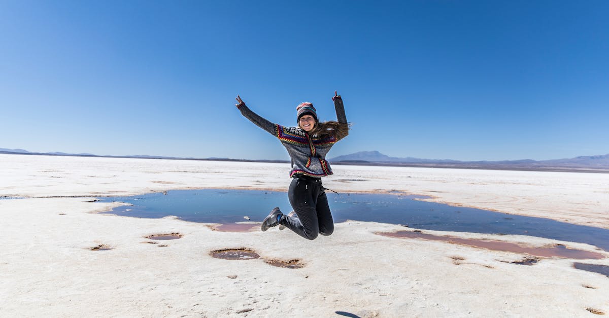 Smiling woman jumps with joy at Bolivia's Uyuni Salt Flats under a clear blue sky.