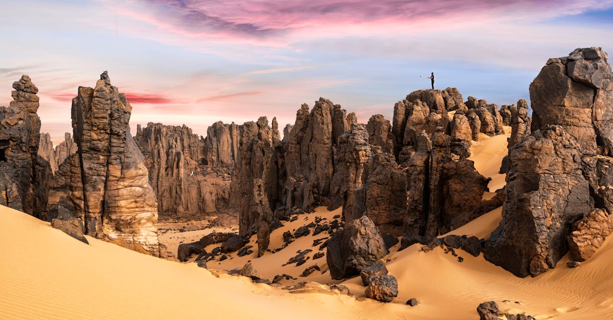 Stunning sunrise over the Hoggar Mountains with dramatic rock formations and a lone hiker.