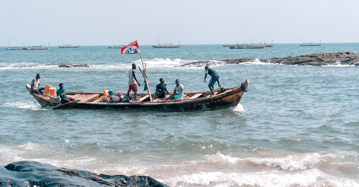 Fishermen navigating a wooden boat on the vibrant Elmina coast, showcasing traditional fishing culture in Ghana.