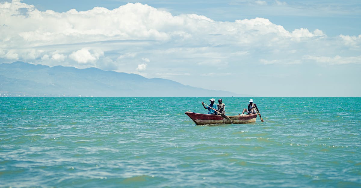 Three individuals in a wooden boat paddling through clear turquoise ocean under a bright sky.