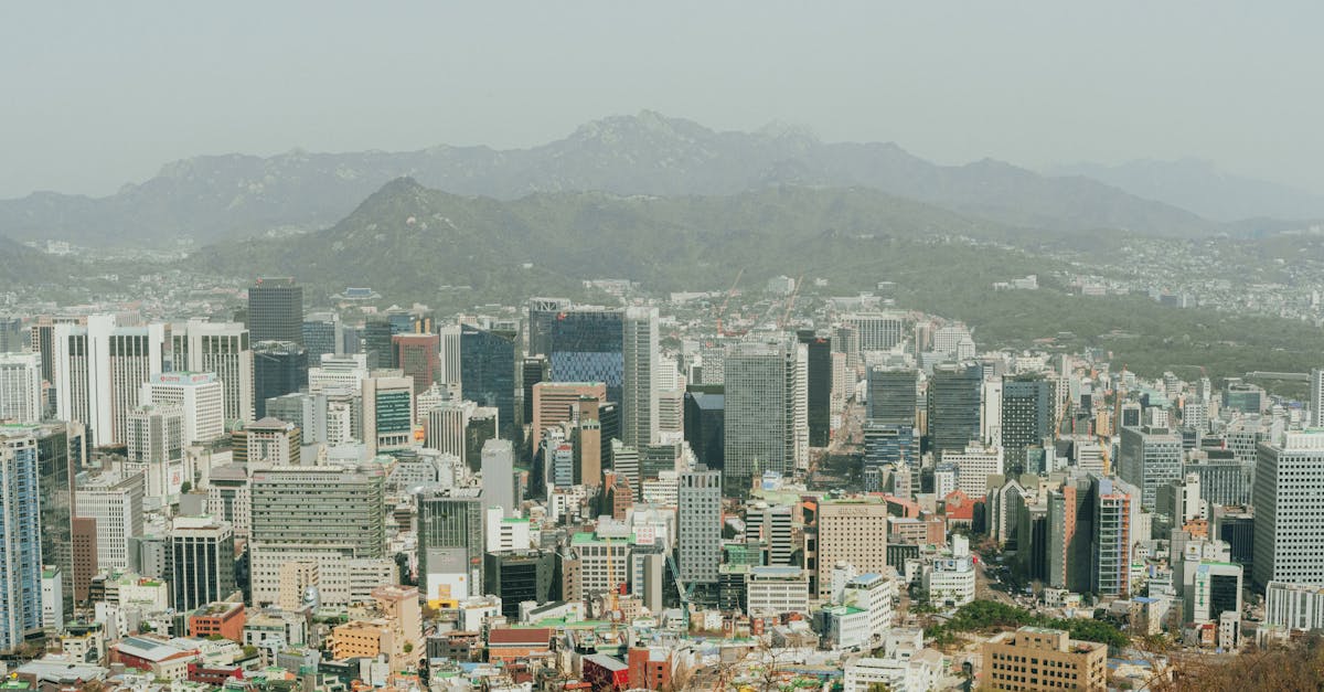 Panoramic aerial view of Seoul's skyscrapers with surrounding mountains, depicting modern urban landscape.