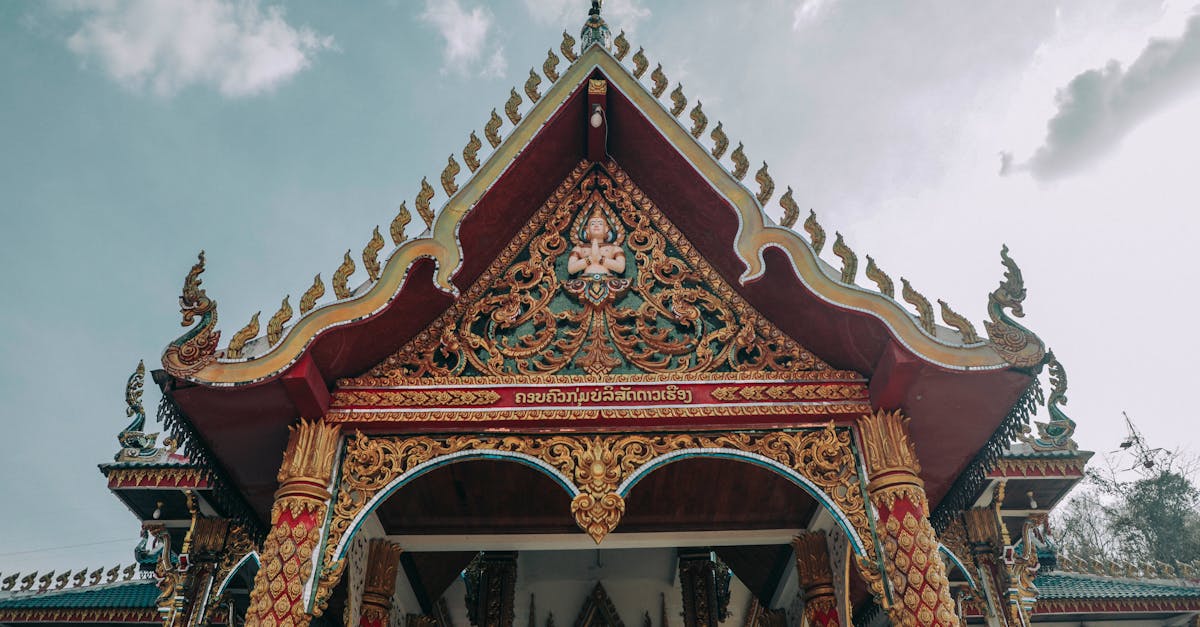 From below of ancient masonry Asian temple facade with ornament on roof and arched entrance under cloudy sky
