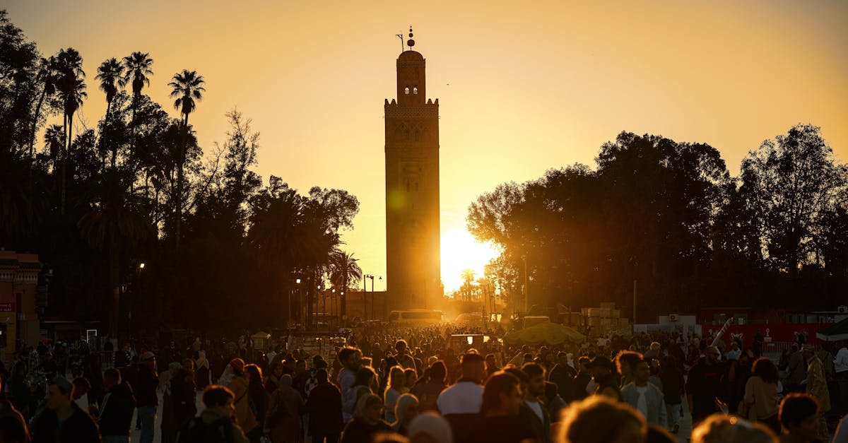 A bustling crowd gathers under the iconic Koutoubia Mosque tower at sunset in Marrakesh, Morocco.