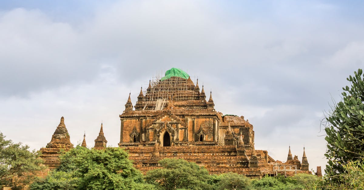 Stunning view of Htilominlo Temple in Bagan, Myanmar, amid lush greenery and cloudy skies.