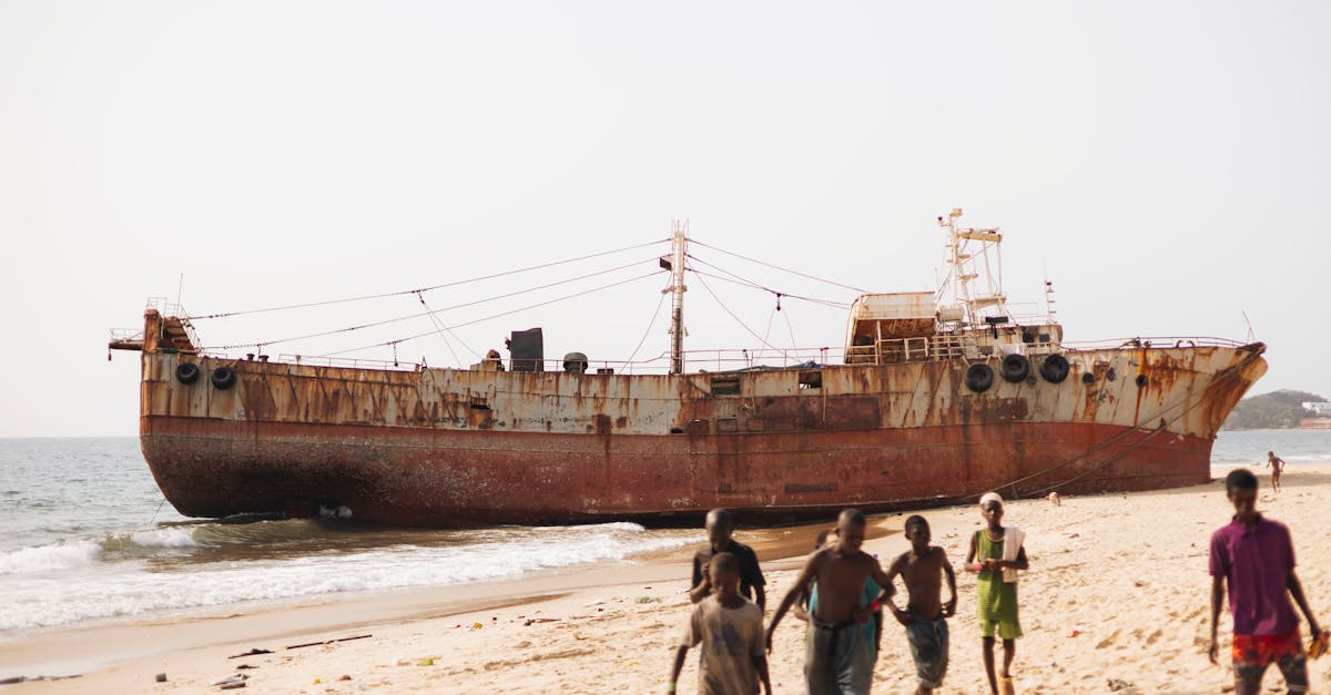Rusty shipwreck on a sunny beach in Freetown with children playing nearby.