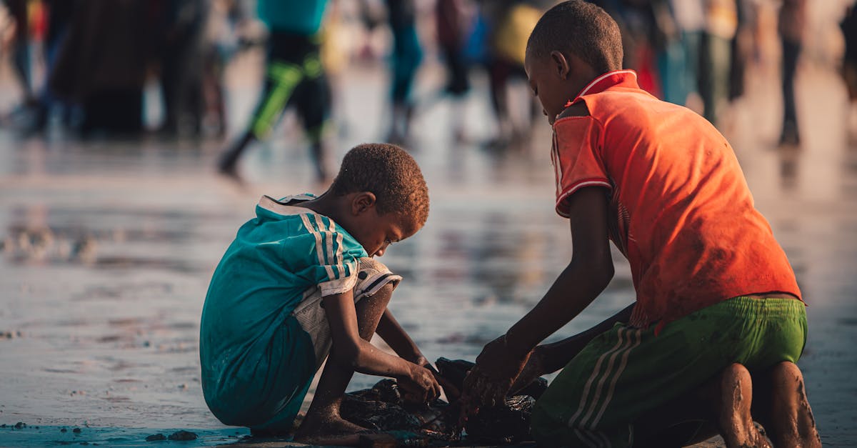 Two children playing on a sunlit Mogadishu beach, surrounded by people.