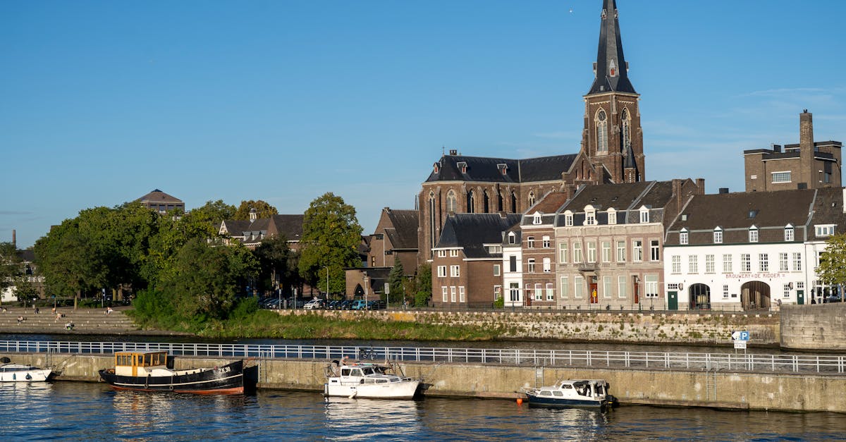 Discover Maastricht's charming riverside with historic buildings and the iconic church under a bright summer sky.