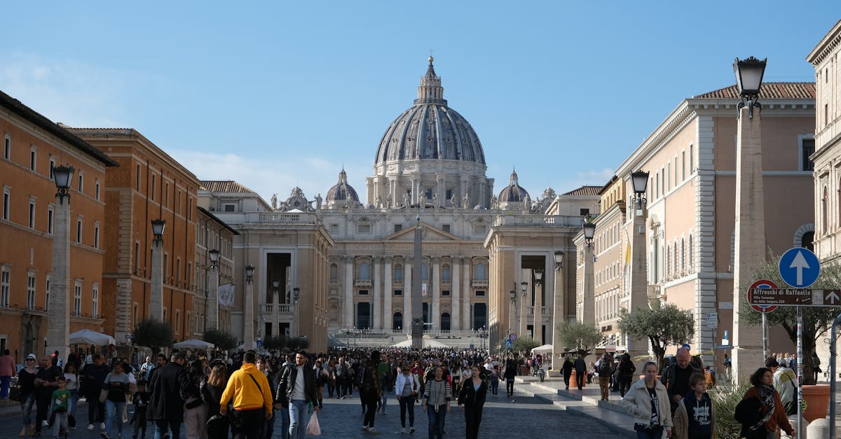 Crowds gather at St. Peter's Basilica, a landmark of Vatican City, under the daytime sky.