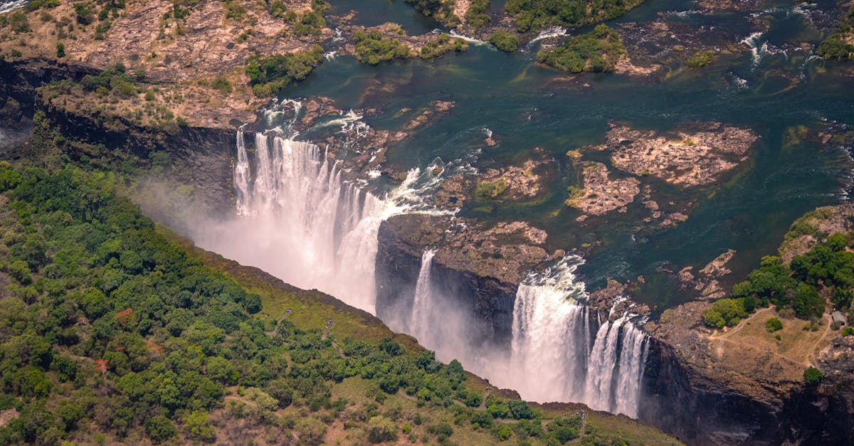 Breathtaking aerial view of Victoria Falls surrounded by lush greenery during summer day.